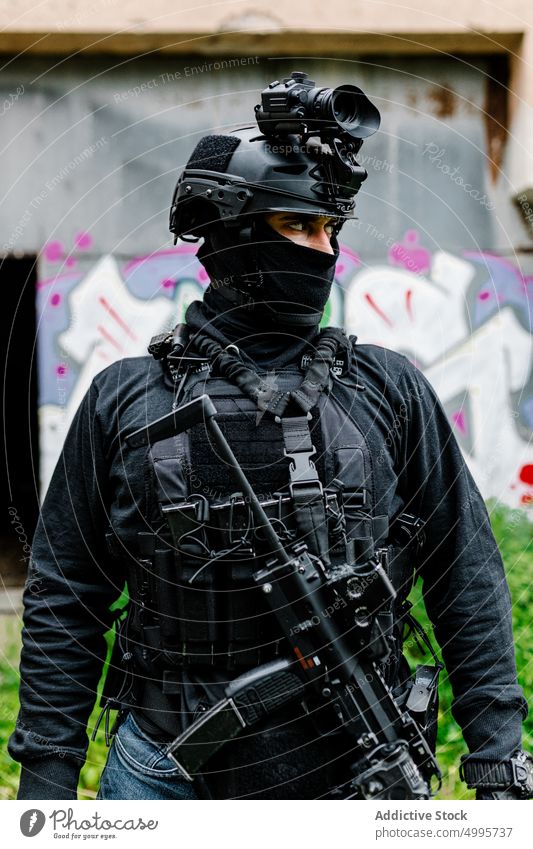 Anonymous warrior in protective costume looking away near shabby construction man attentive serious fighter military graffiti weapon confident combat brave