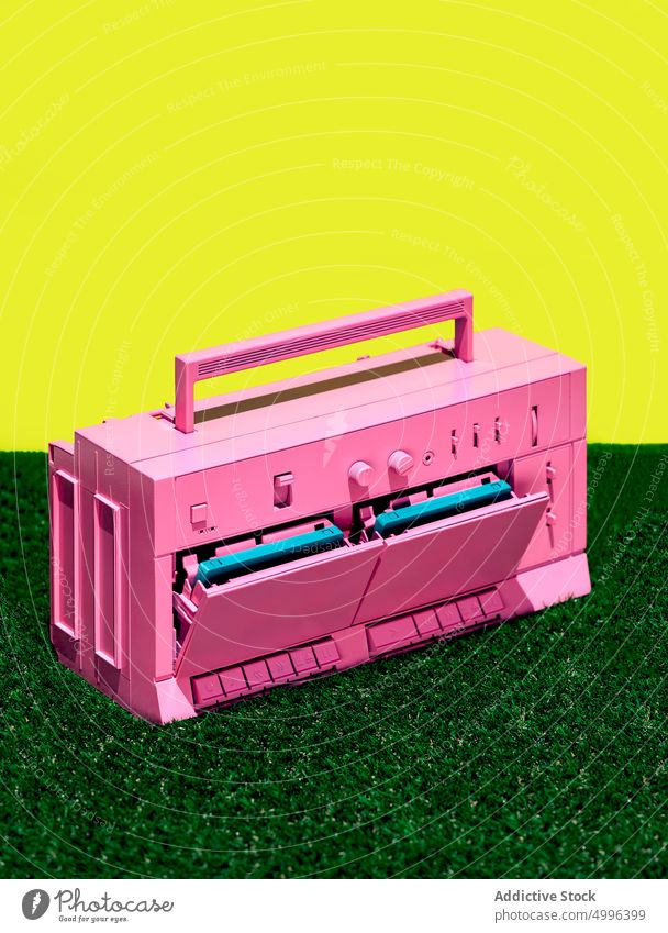 Pink retro tape recorder on grass in studio colorful bright vintage cassette player music stereo old fashioned vivid vibrant audio sound style melody song