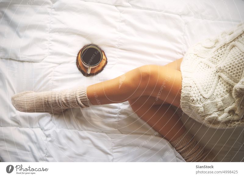 Soft photo of woman on the bed with cup of coffee, top view point lazy sunday winter morning girl home relax socks beautiful young bedroom female white cozy