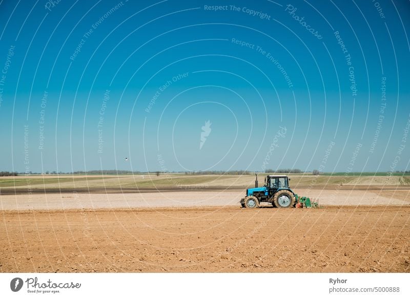 Tractor Plowing Field In Spring Season. Beginning Of Agricultural Spring Season. Cultivator Pulled By A Tractor In Countryside Rural Field Landscape Under Clear Sunny Spring Blue Sky. Skyline