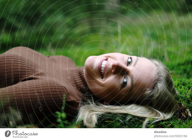 Young blonde woman with dimples lies on the moss in the forest and smiles at the camera from the side Young woman Woman Blonde Feminine pretty fortunate
