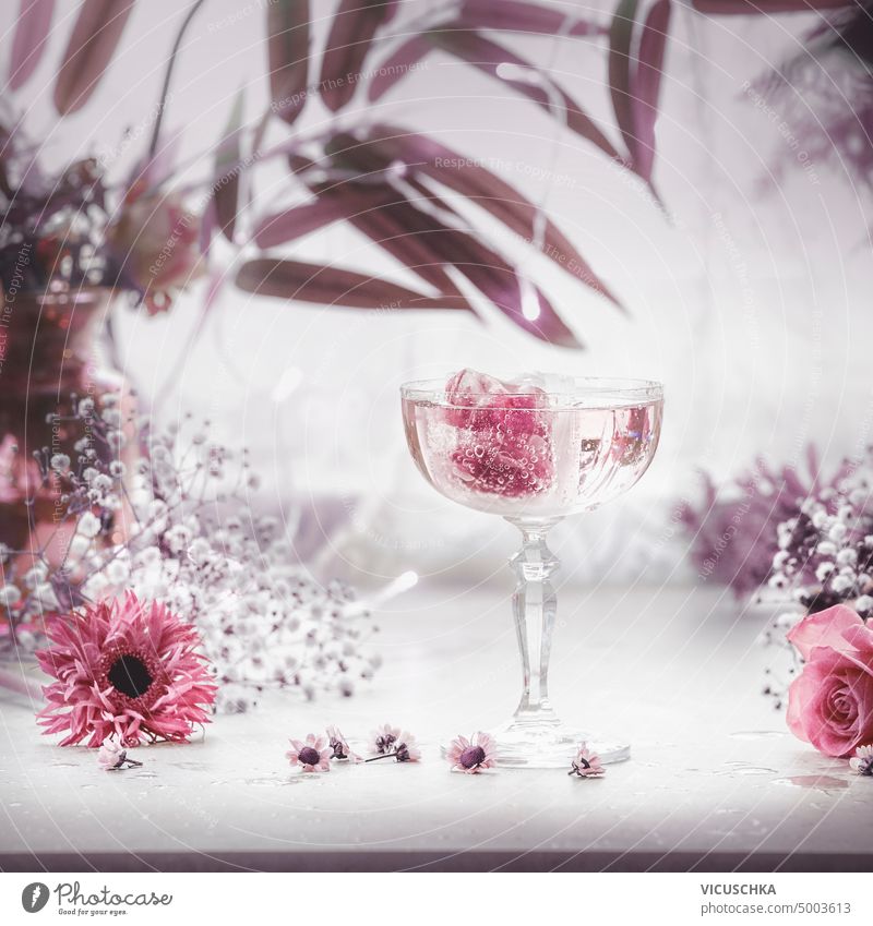 Fancy drink in wide glass of champagne with pink ice cubes and and purple flowers and leaves. fancy arrangement event elegant rose romantic table fancy glasses