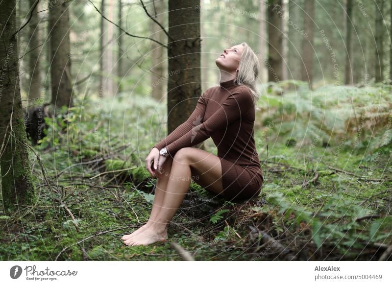 beautiful blonde woman with bare legs and sheer blouse sits crosswise on  brown armchair in front of turquoise wall - a Royalty Free Stock Photo from  Photocase