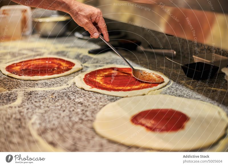 Crop chef cooking pizza in restaurant man tomato sauce smear kitchen tradition prepare male spoon spread ingredient italian cuisine process food pizzeria recipe