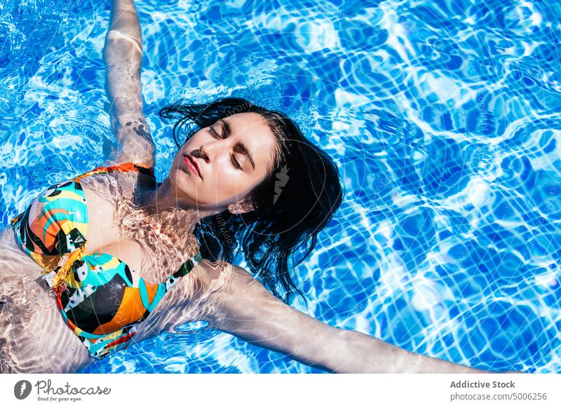 Young woman relaxing in outdoor pool in summertime poolside float chill enjoy carefree water sunbath female bikini colorful sunlight swim aqua resort vacation