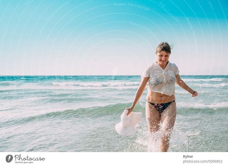 Young Caucasian Lady Woman In Swimsuit And Summer Hat Running In Sea Water Splashes. Vacation On Sea Ocean Beach Aegean Sea active active lifestyle attractive