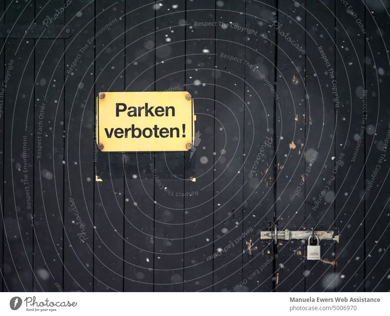 Trickling snow in front of a dark garage door with a sign that says "No Parking!" no parking Clue interdiction Garage Parking lot car Transport Goal Lock