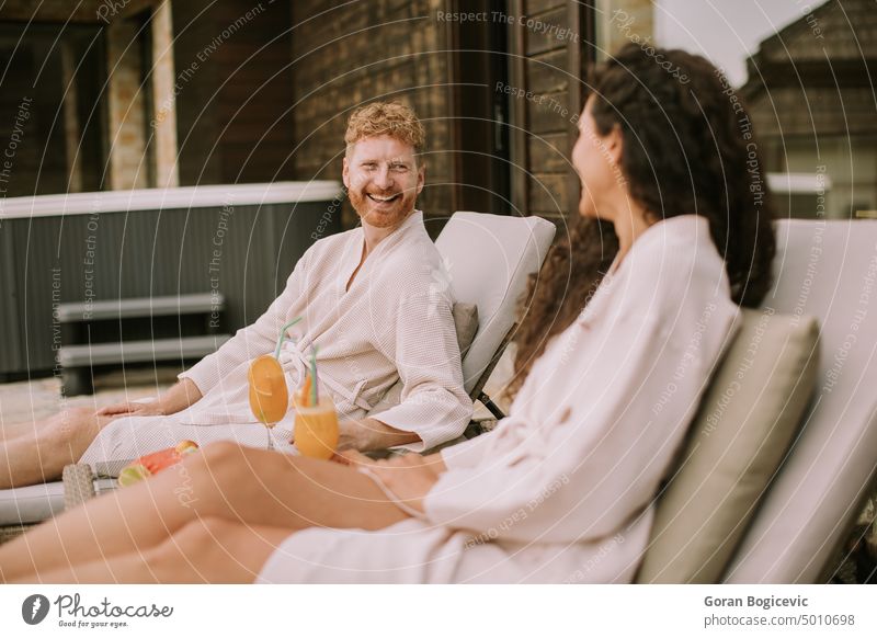 Young couple relaxing on beds and drinking fresh orange juice on the outdoor terrace romance caucasian happy togetherness husband female lying couple in love