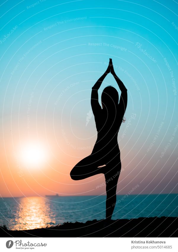 Young slim girl practicing yoga on mountain against ocean or sea at sunrise time. Silhouette of woman in rays of awesome sunset. silhouette beach body exercise