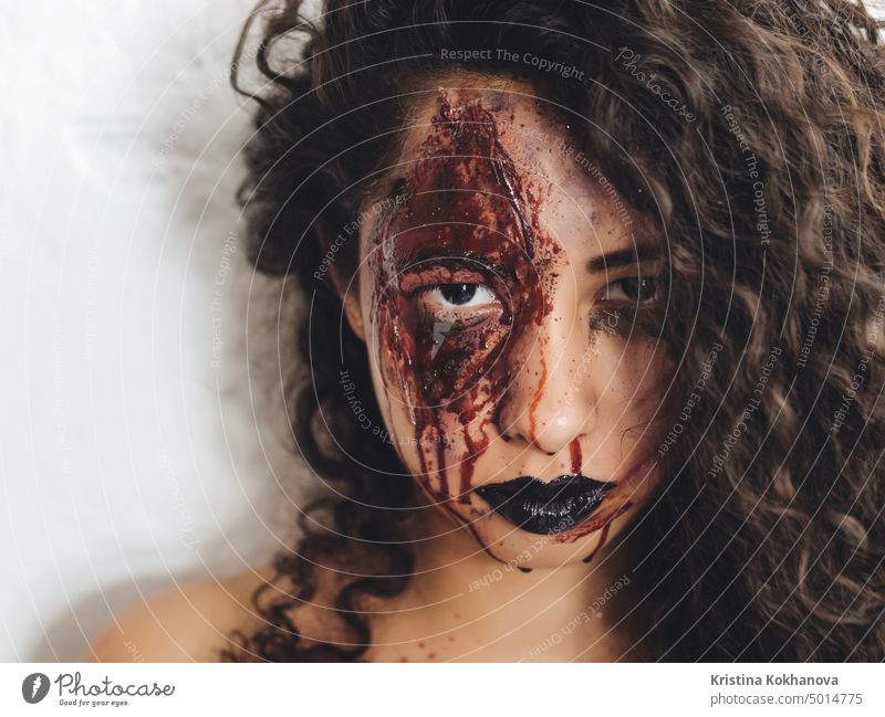 Scary portrait of young zombie woman with Halloween blood makeup. Beautiful latin beaten girl with curly hair looking into camera. adult art artist beautiful