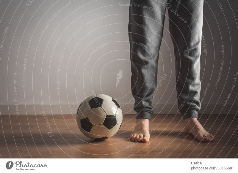 Legs of a man standing next to a football soccer legs room indoors barefoot feet male unrecognizable adult person sports white wall people active recreation