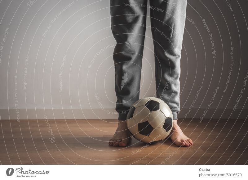 Legs of a man standing in front of a football soccer legs room indoors barefoot feet male unrecognizable adult person next to sports white wall people active