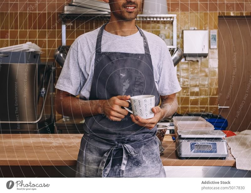 Male baker with cup of coffee coffee break man cook relax enjoy refreshment apron male wooden table dirty lean work bakery job drink beverage guy hot drink mug