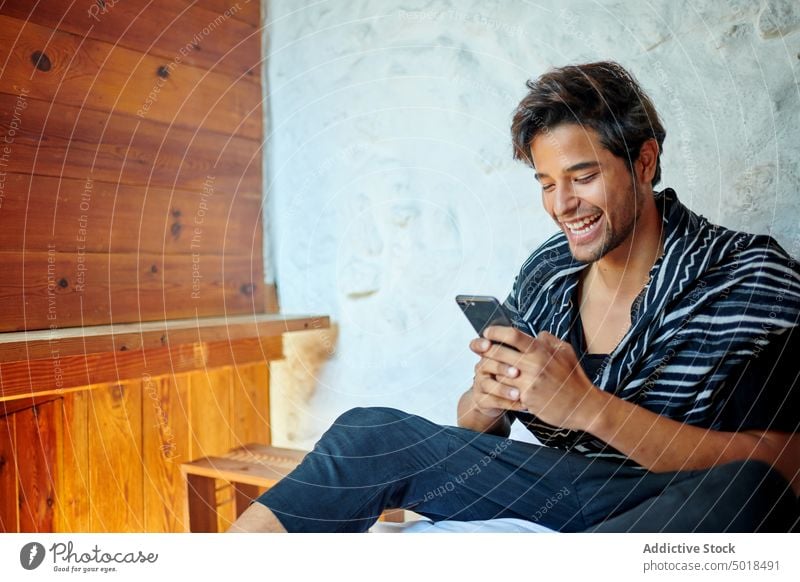 Stylish Hispanic man chatting on smartphone on bed stylish masculine internet macho portrait using device watching cellphone gadget surfing online