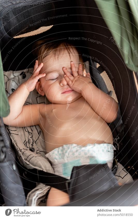 Infant lying in stroller with hands in face baby sleep hand in face adorable shirtless rest innocent childhood babyhood infant diaper toddler tender sweet