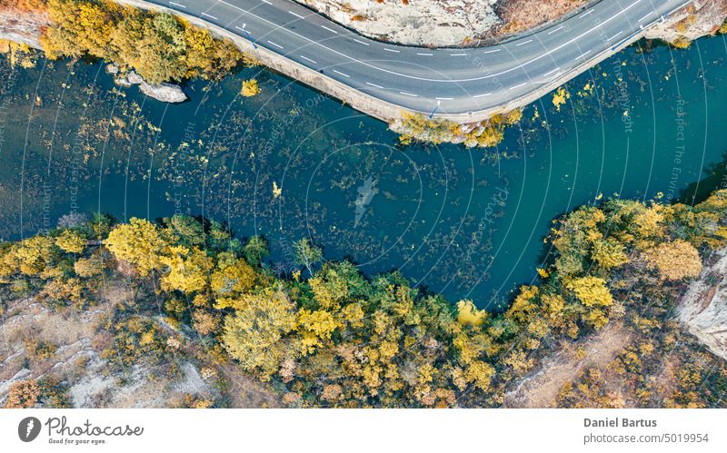 A road on a mountain slope overlooking a river with colorful vegetation and trees on the edge of the slope. Drone flight view. Background autumn background
