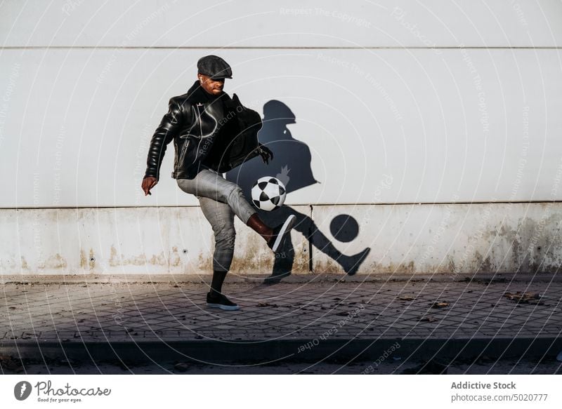 Black man kicking ball on street black african american jumping wall grungy football game activity male pavement sidewalk exterior building style trendy casual