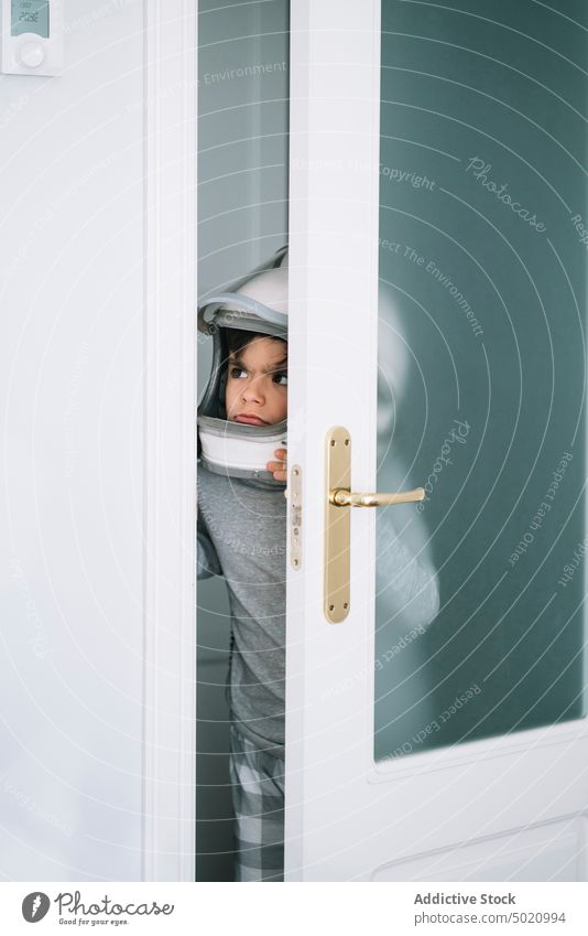 Adorable kid with helmet looking through the crack in the door astronaut background boy child childhood concept creation handmade heating thermostat imagination