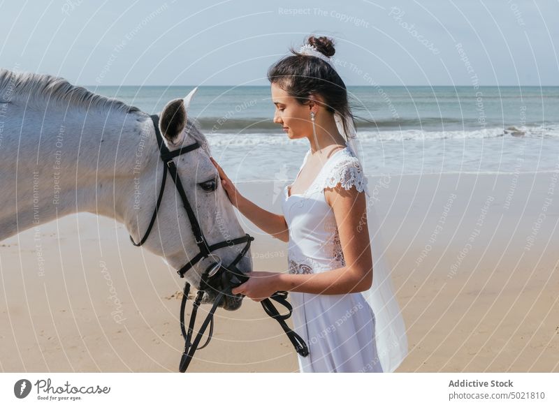 Calm bride with horse on the sea beach white dress animal equine celebrate wedding seashore woman walk pretty veil barefoot elegant style festive bridal