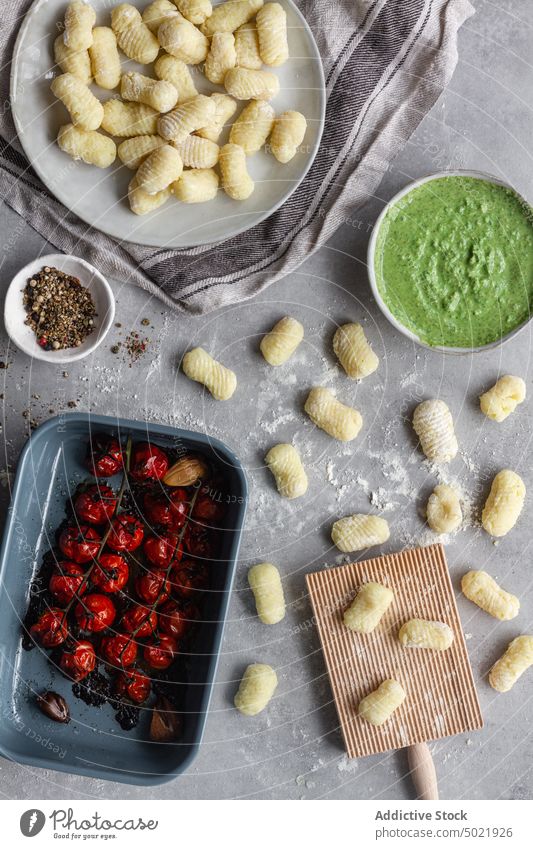 Raw gnocchi near cooking ingredients and tools dough potato table kitchen pepper flour board pasta plate ribbed prepare food recipe cuisine raw culinary meal