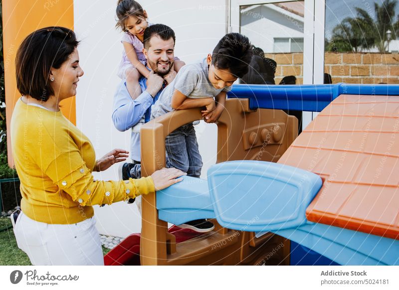 Joyful ethnic family playing on slides on playground backyard mother father children together joy happy spend time childhood motherhood fatherhood