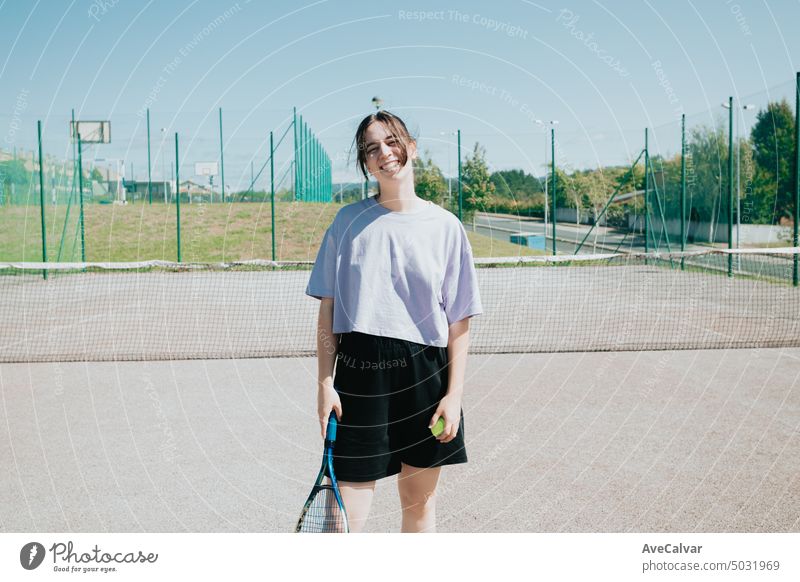 Frontal portrait of a tennis woman player at the court smiling cheerful to camera, learning sports game match training person racket female action athlete