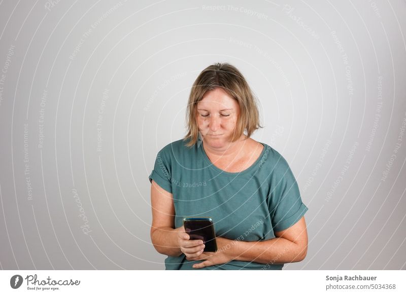 A woman with abdominal pain holds a smartphone in her hand. Emergency call. Woman Stomach pain Interior shot Healthy Pain 50 plus Hand spasm Distress Help stop
