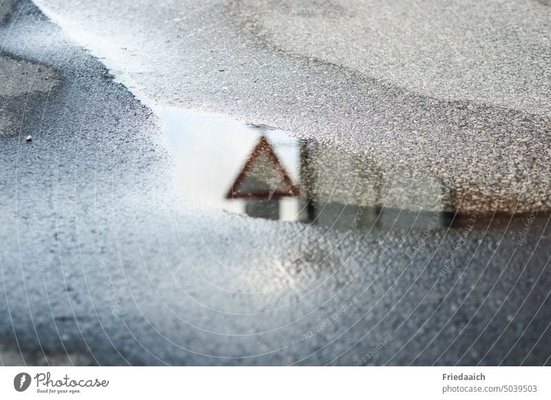Reflection of a traffic sign in a puddle in the asphalt puddle mirroring Asphalt Transport Road sign after the rain Street give right of way Water Puddle Wet