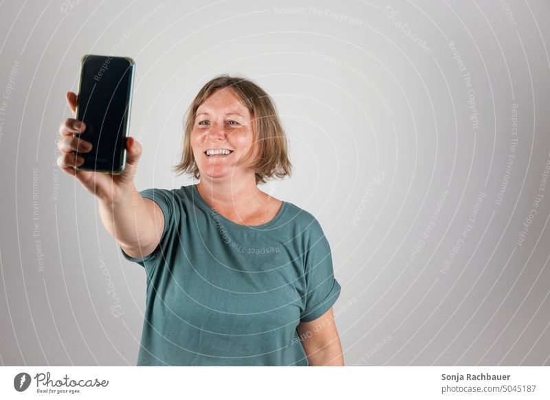 A woman over 50 takes a selfie with a smartphone Woman Selfie Lifestyle Smiling Cheerful Studio shot 50 plus Happiness Happy fun Technology free time Cellphone