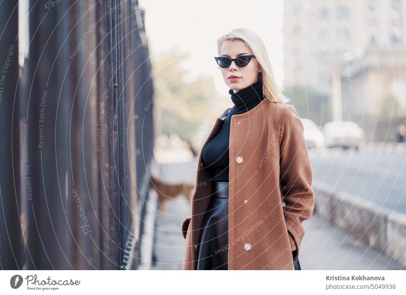 Portrait of young blonde businesswoman in autumn city. Girl have stylish look, sunglasses and nose piercing. Lady walking on the street alone. Fashion concept