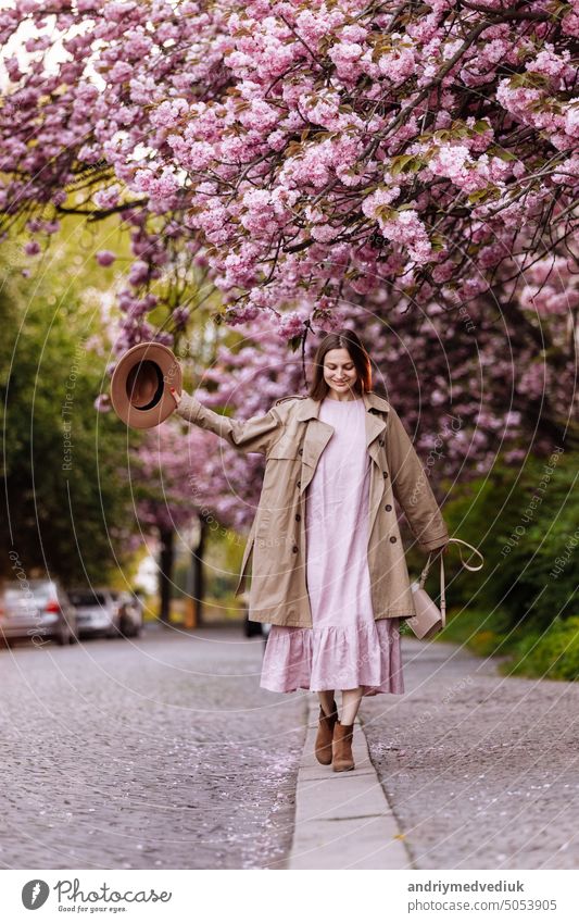 young beautiful stylish woman in hat and pink dress walking near sakura flowers in the park. Spring concept. Uzhhorod, Ukraine spring fashion beauty girl