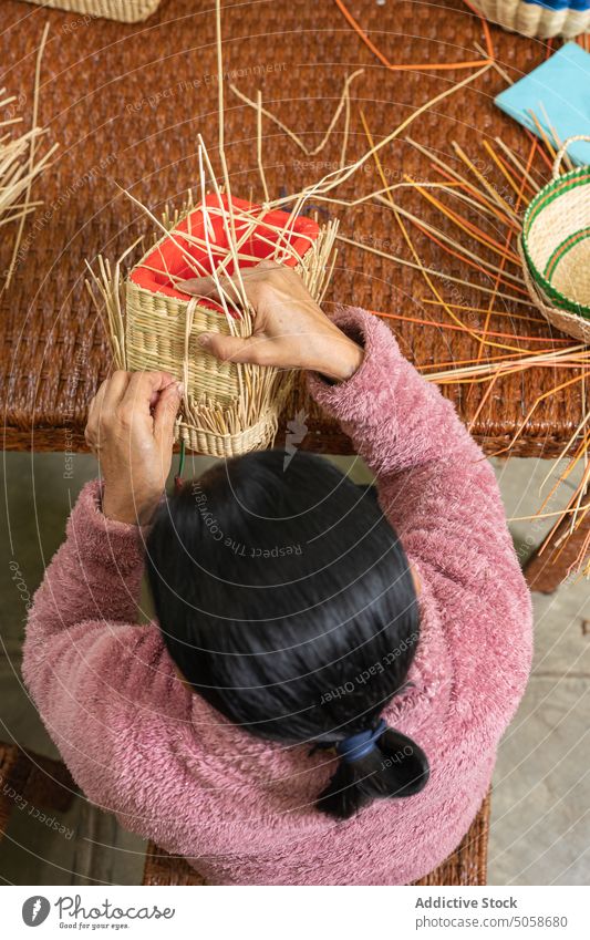Anonymous female artisan making straw basket craftswoman weave table workshop handmade dry skill basketry mature middle age small business workplace handicraft