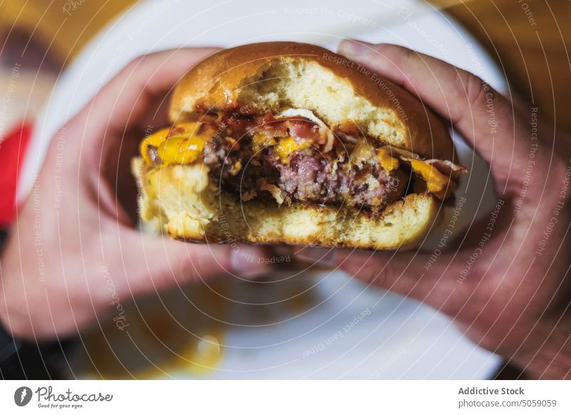 Unrecognizable person eating delicious burger hamburger fast food tasty appetizing scrumptious cheese plate meal lunch yummy patty dish table meat hungry