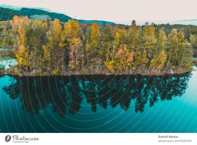 The reflection of trees in autumn on the water surface, colorful yellow-orange leaves. The forest reflecting in the water surface. Blue-turquoise lake water.