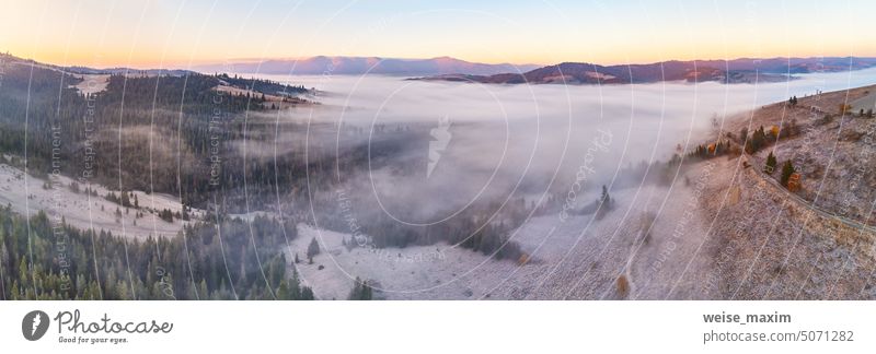 Mountain autumn misty Sunrise panorama. Majestic Morning fog, November Valley Aerial scene. Ice, frost on grass. Fall sunny Landscape, forest hills. Beautiful tonal perspective