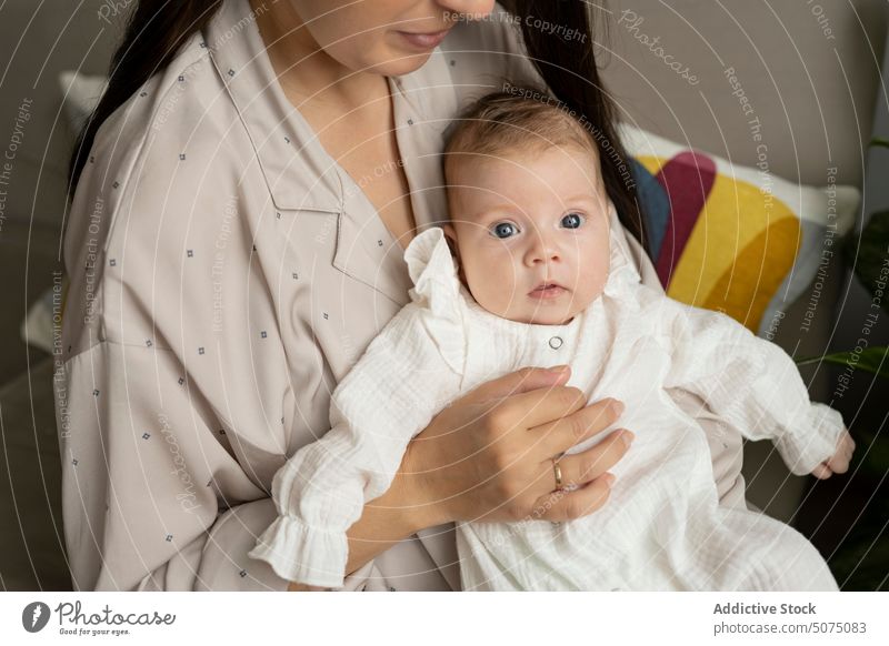 Anonimous young mom caressing infant mother baby hug sofa living room home love morning female tender peaceful pajama fondness parent together newborn comfort