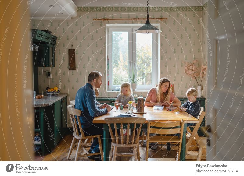 Happy young family at dining table at home together real life real people bonding indoors quality time house parenting kids enjoyment fun happy togetherness
