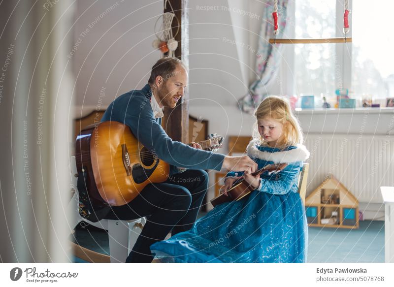 Dad teaching his daughter how to play guitar modern manhood genderblend real life real people bonding family indoors quality time house parenting kids enjoyment