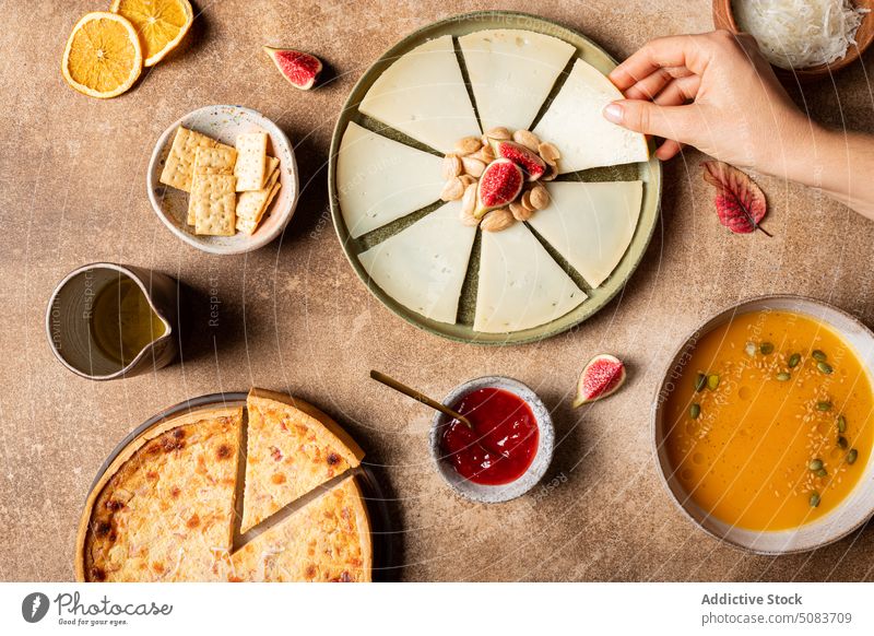 Crop woman taking piece of cheese from plate table nut fig sauce cracker soup female pumpkin seed citrus orange serve leaf fruit dish fresh food tasty delicious