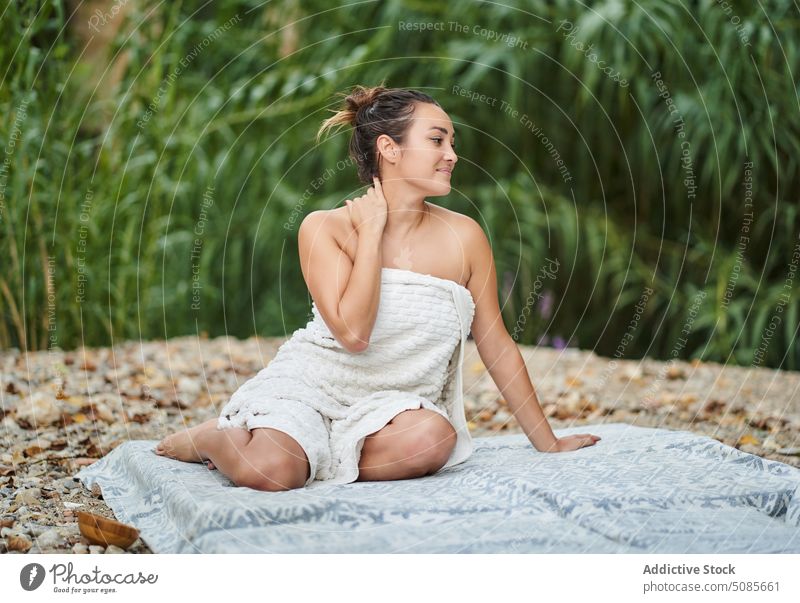 Woman in towel sitting on mat in park woman blanket harmony relax naked smile nature summer plant tropical female happy touch neck optimist green garden holiday