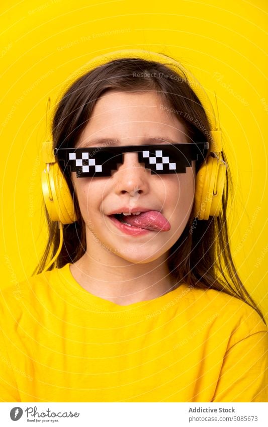 Girl in headphones and pixel glasses girl kid listen music studio shot tongue out device smile enjoy positive cheerful schoolgirl child gadget style yellow