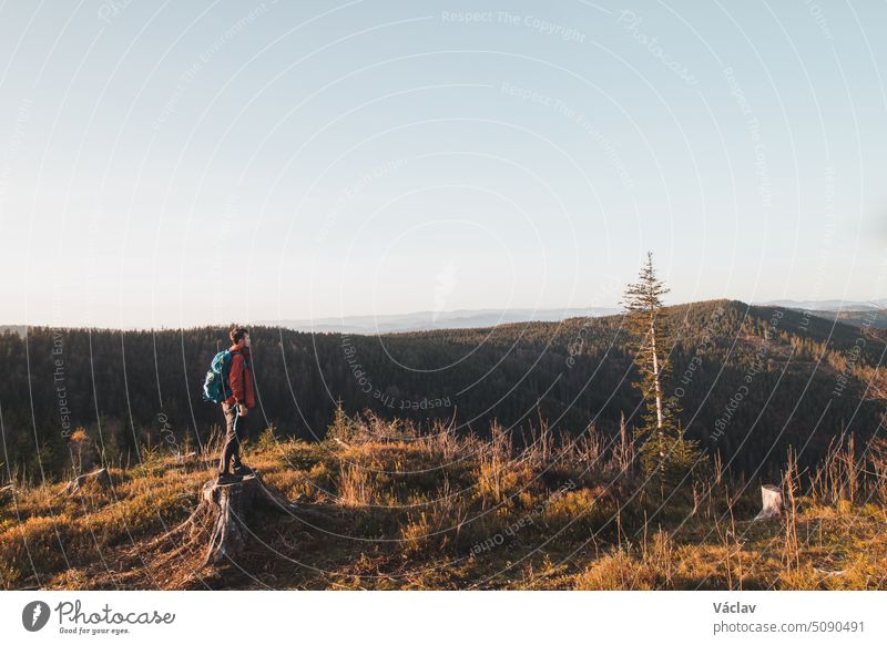 An active hiker enjoys the feeling of reaching the top of the mountain at sunrise. A hiker is illuminated by the morning sun and enjoys the view of the valley. Beskydy Mountains, Czech Republic