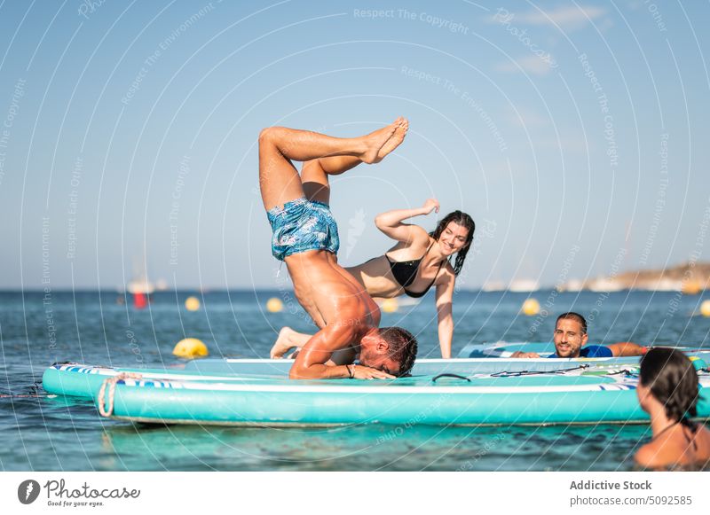 Cheerful friends watching man performing headstand on paddleboards people cheerful sup board yoga happy support sea summer hobby water women recreation show