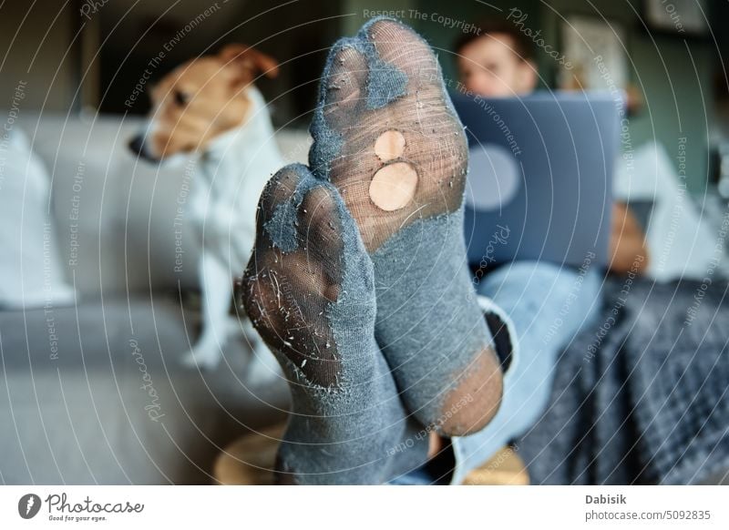 Man with leaky socks resting on sofa near dog, using laptop man leg hole work crisis people freelancer poor money home concept clothes clothing jeans human feet