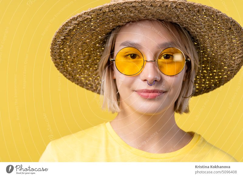 Portrait of young pretty blonde woman on summer yellow studio background. Confident sunny outfit with sunglasses and straw hat. adult beautiful female happy