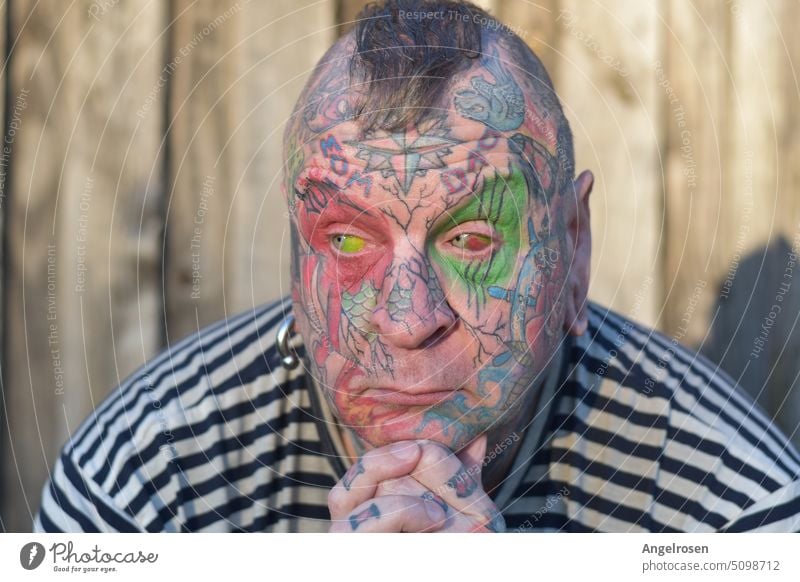 A man completely tattooed in the face, with a thoughtful expression. Even his eyeballs are not white, because they are colored by means of eyeball tattoo.