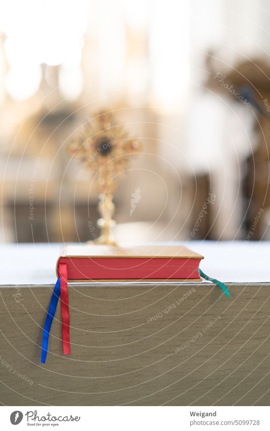 Close up of Bible or hymnal with red cut and colorful ribbons on an altar in front of a blurred cross in the background when light falls on it Church Song book