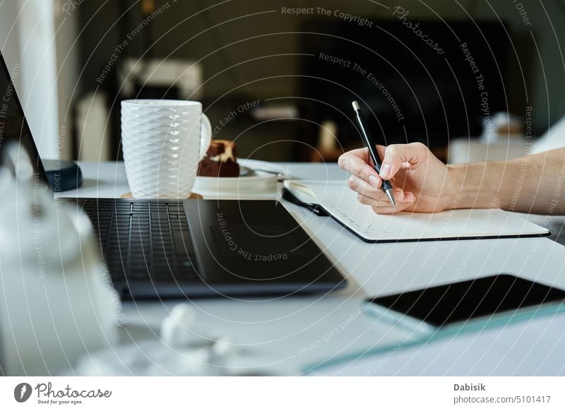 Designer draws sketch on paper, sits at desk with laptop in front of window woman work from home hand workplace creative remote freelance office workspace