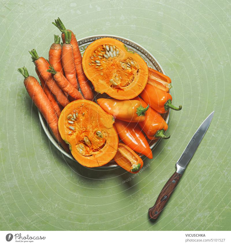 Plate with orange vegetables: carrots, pumpkins, paprika on green background with knife, top view. Healthy food, plate healthy food diet cooking overhead