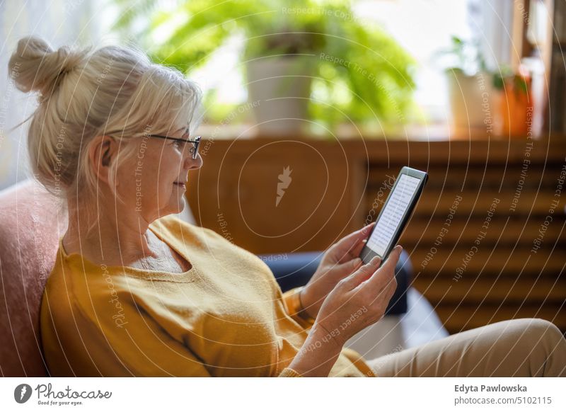 Senior woman using e-reader and reading an e-book at home smiling happy enjoying positive people senior mature female elderly house old aging domestic life